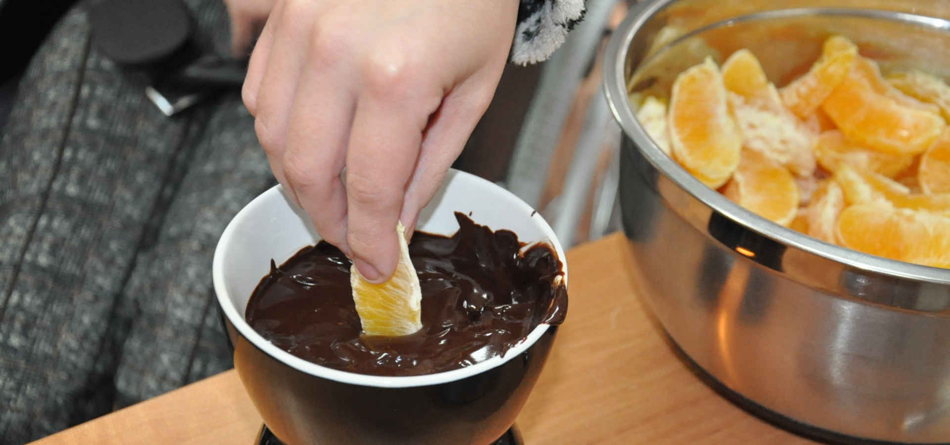 Dłoń zanurzająca pomarańczę w czekoladzie
