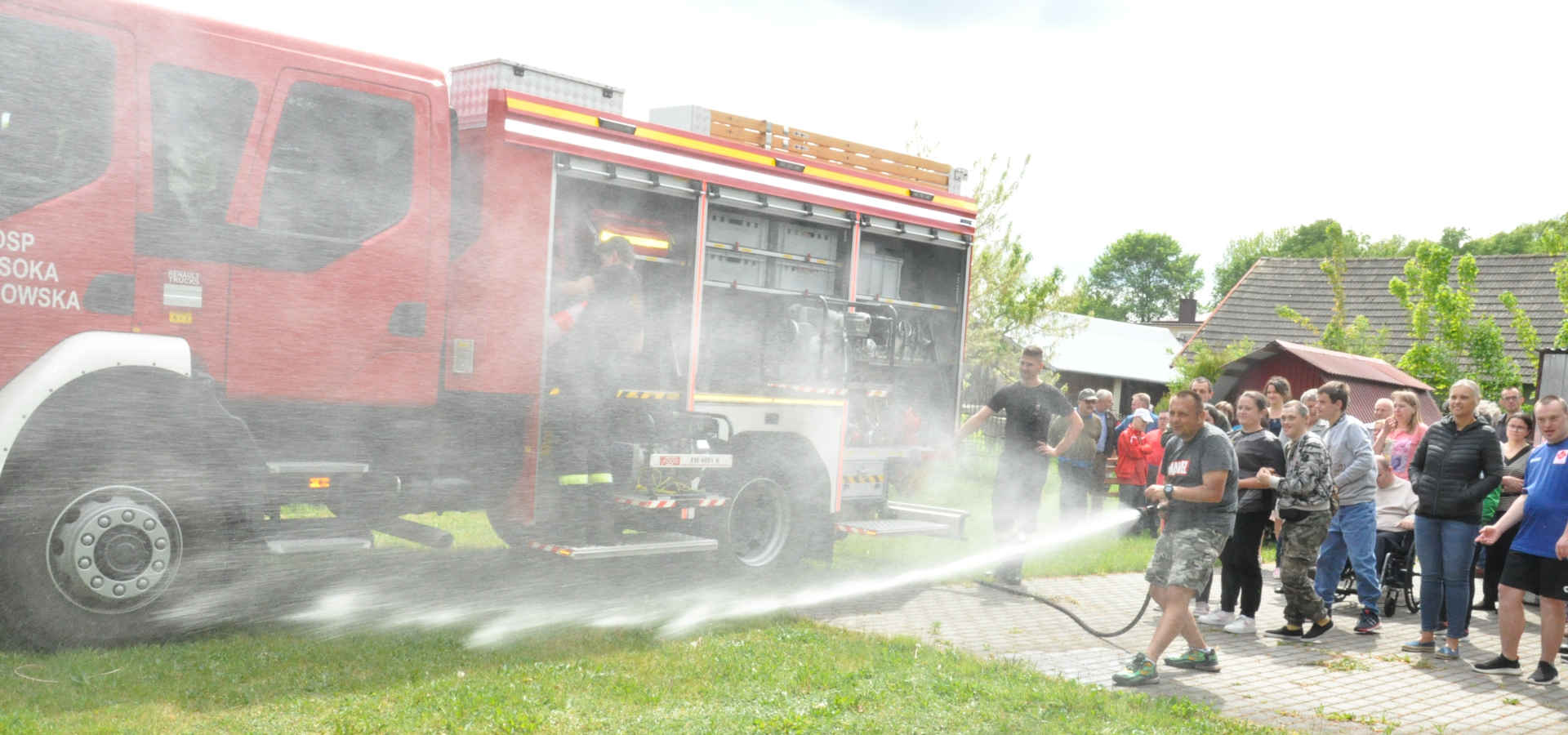 Uczestnicy pikniku przy wozie strażackim leją wodą